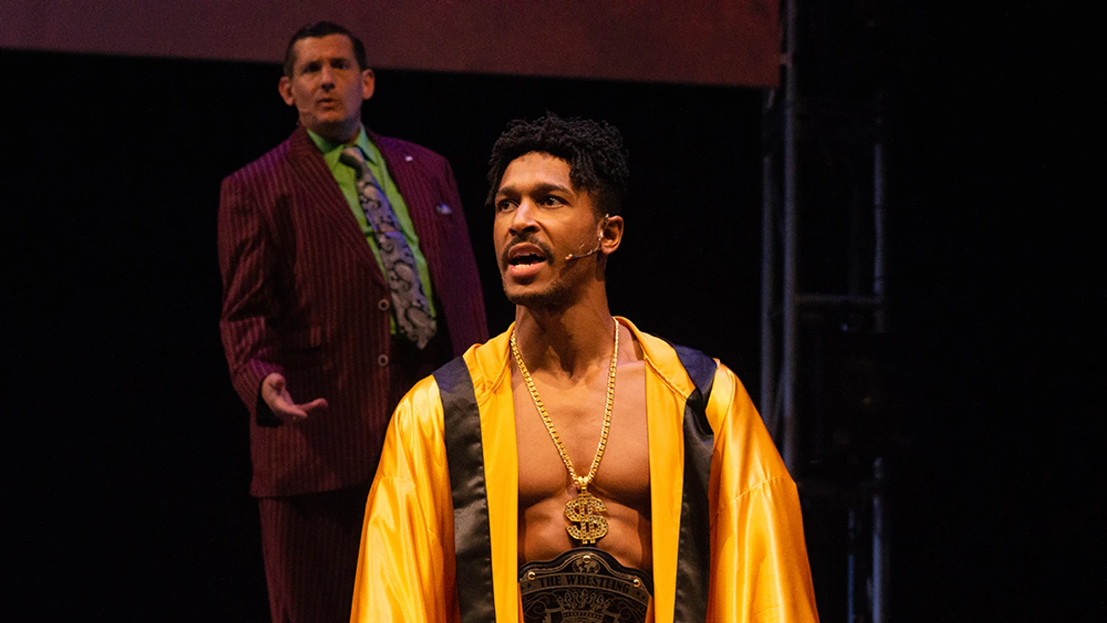 Wrestler in gold robe with man in purple suit behind him.